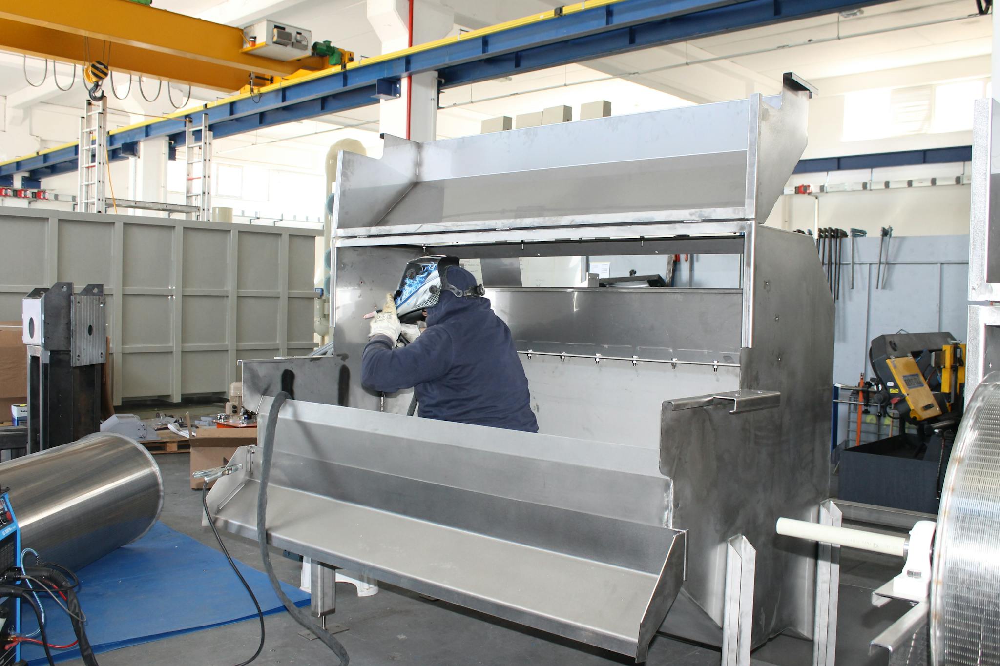 A worker welds metal components inside a large industrial factory.