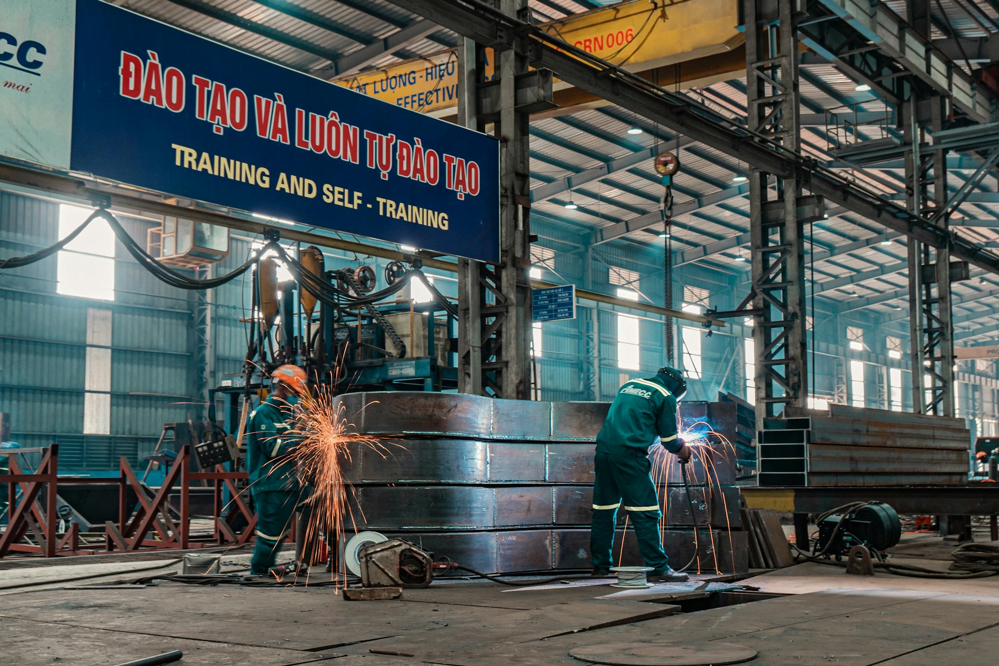 Workers weld metal structures in a bustling industrial factory, showcasing a dynamic work environment.