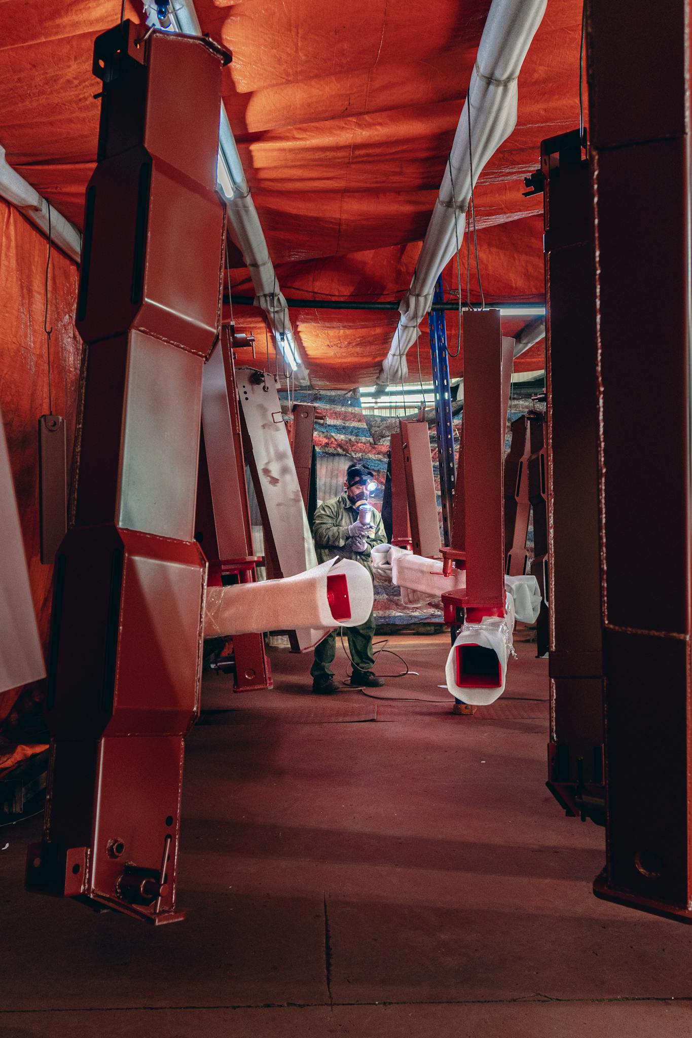 Welder working amid suspended metal structures in a factory setting.